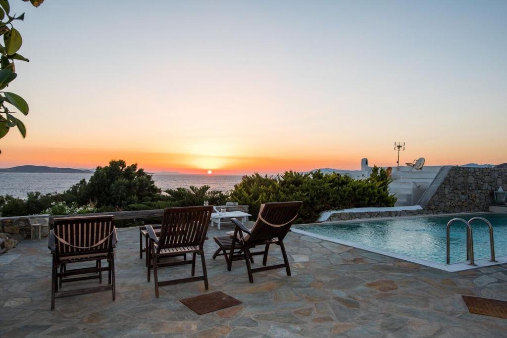 a patio with chairs and a swimming pool with a sunset at Villa Waves in Agios Ioannis Mykonos