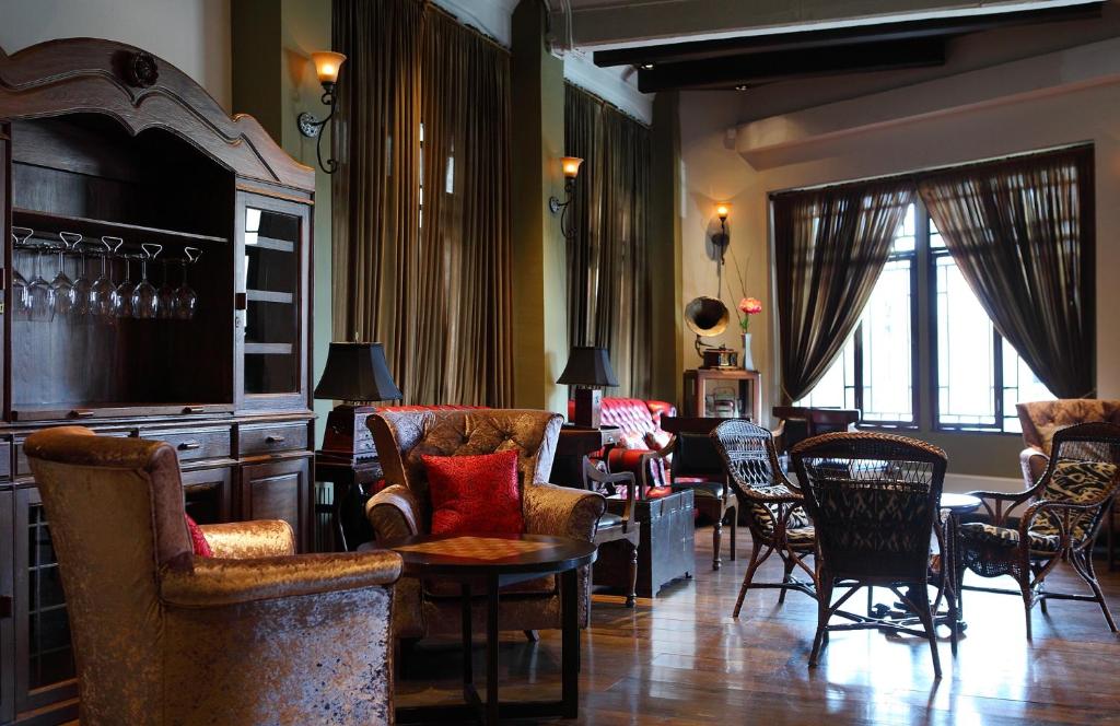 A richly furnished lounge with armchairs, rattan seating, a bar cabinet and tall curtained windows.
