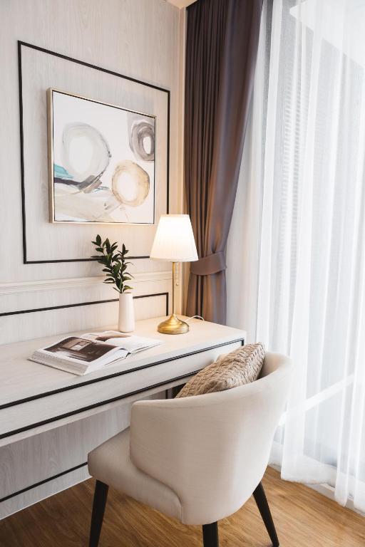 A light-colored desk and lounge chair beside a tall curtained window.