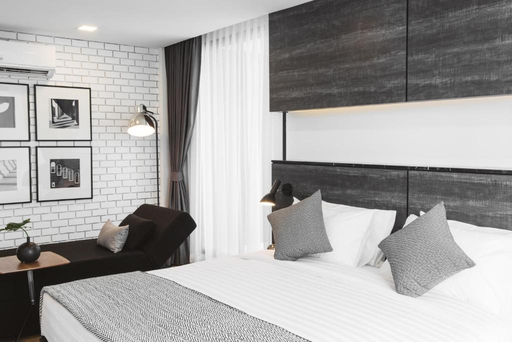 A bright bedroom combines a large bed, black chaise lounge, framed artwork and layered window curtains.