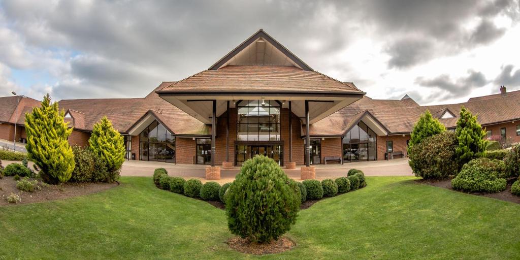 a large building with a grass yard with bushes at East Sussex National Hotel, Golf Resort & Spa in Uckfield