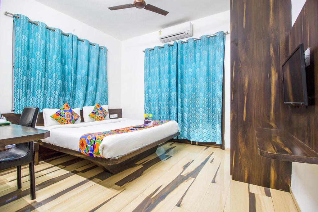 a bedroom with a bed with blue curtains and a desk at FabHotel Pruthamesh Pride in Nashik