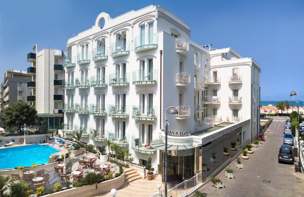 a large white building with a swimming pool in front of it at Hotel Ambassador in Rimini