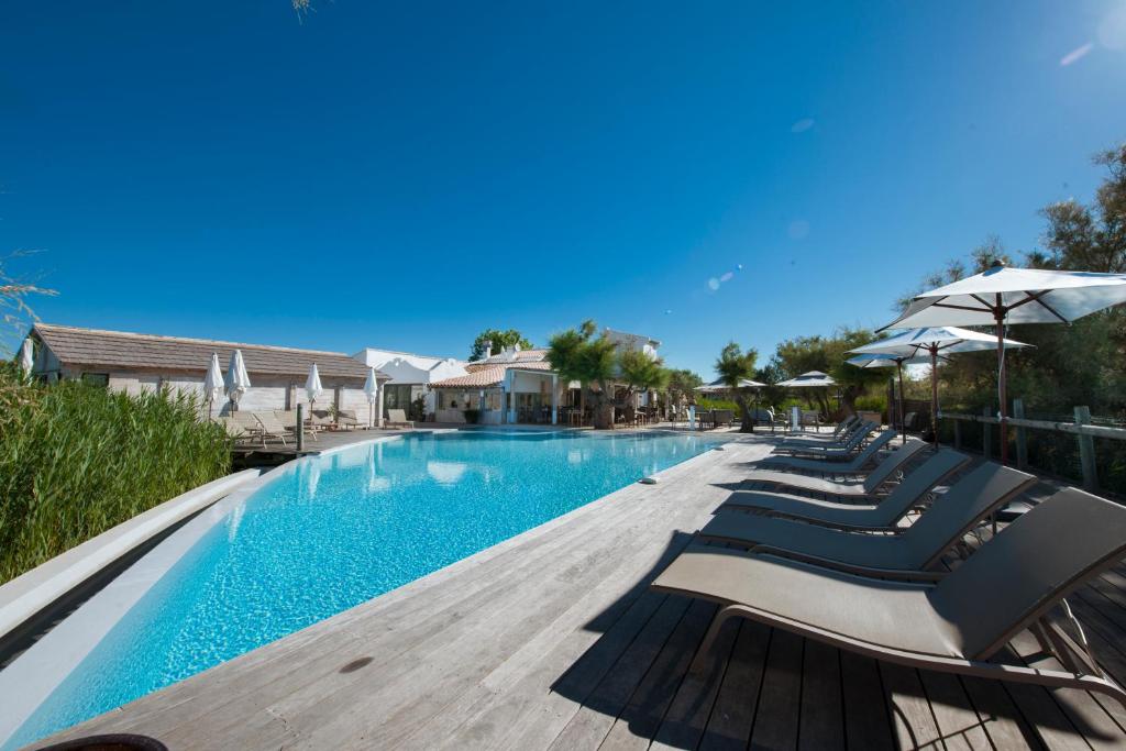 a swimming pool with lounge chairs and umbrellas at Hôtel Restaurant Les Arnelles in Saintes-Maries-de-la-Mer