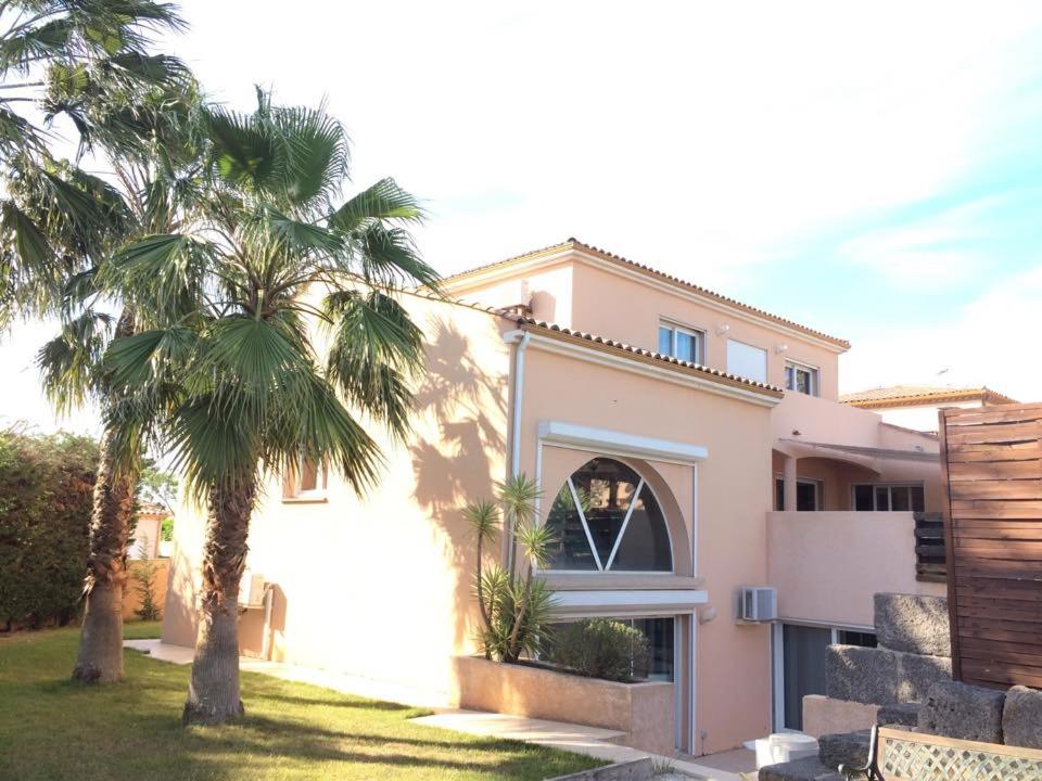 une maison rose avec des palmiers devant elle dans l'établissement Le Mas Des Oliviers, à Agde