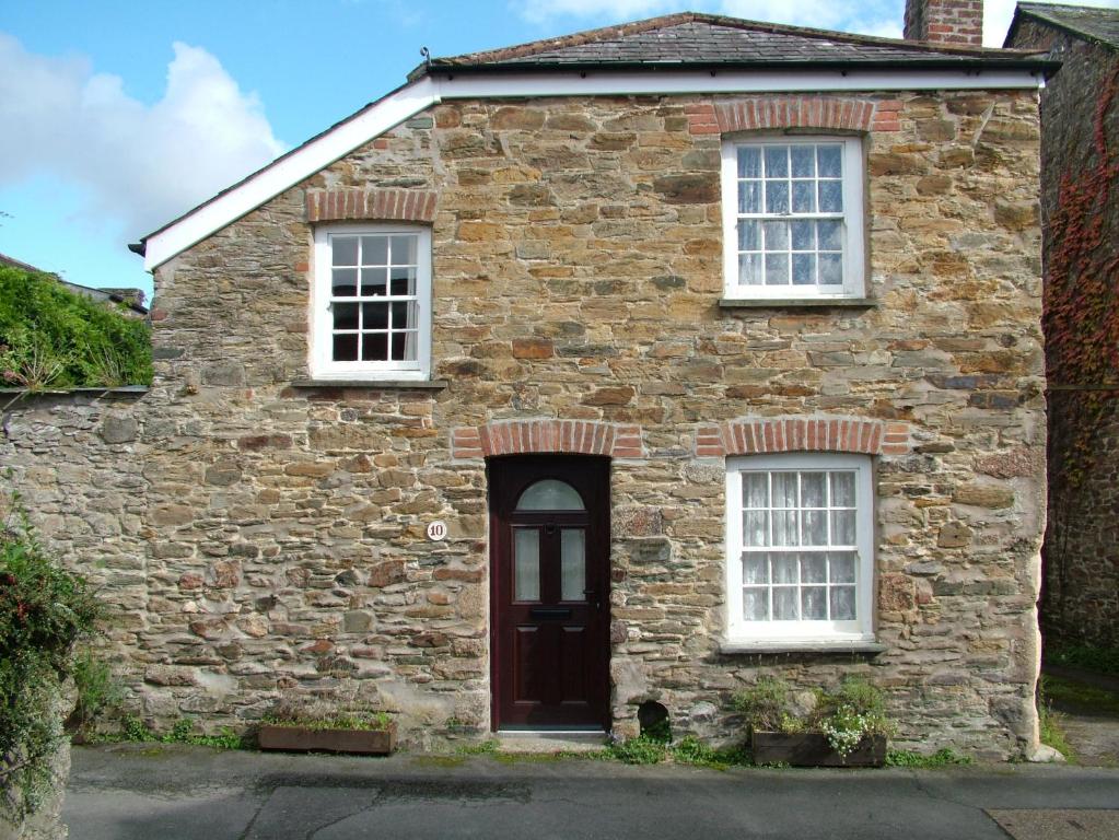 ロストウィジエイにあるGeranium Cottage, Lostwithielの赤い扉と窓が2つある古い石造りの家