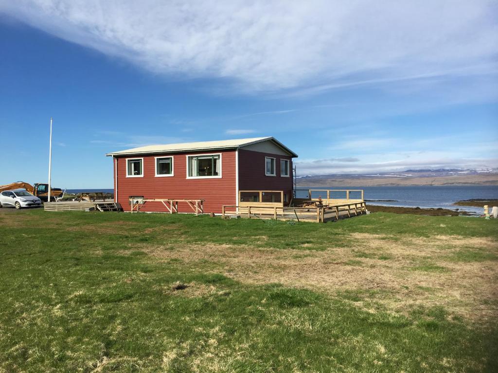 a small red house on a field next to the water at Borgir - The House by the Sea in Borgir