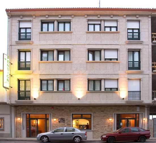 un edificio con dos coches estacionados frente a él en Hostal Restaurante Teodora, en Arzúa