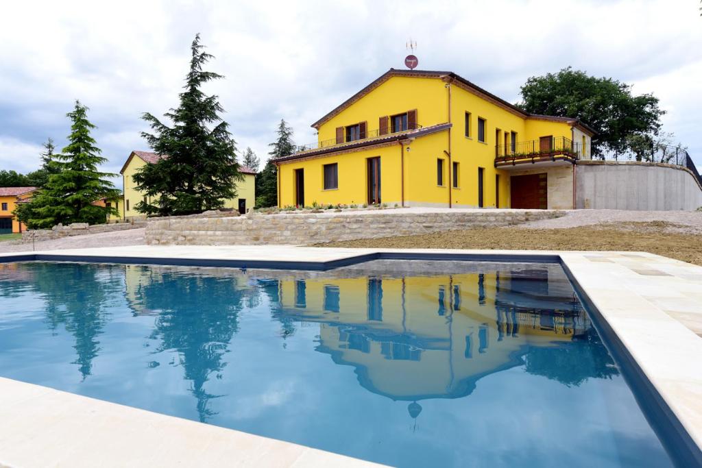een geel huis met een zwembad ervoor bij La Cerqua in Arcevia