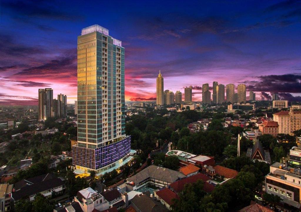 a city skyline with a tall building at dusk at Oakwood Suites La Maison Jakarta in Jakarta