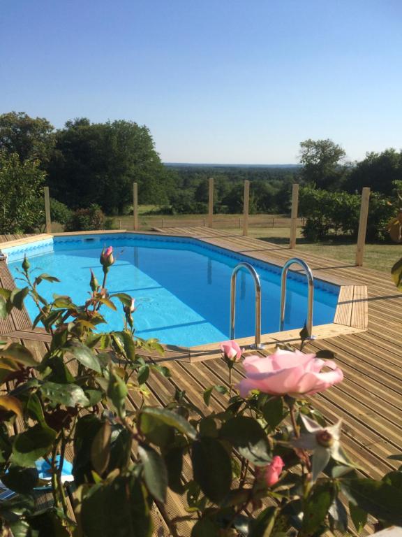 a swimming pool with a wooden deck and a pink rose at Les petits chenes in La Pellerine