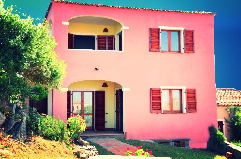 a pink house with red shutters on it at da mario e maria in Aglientu