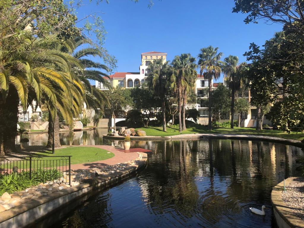 a pond in a park with palm trees and buildings at Island Club Portifino in Cape Town