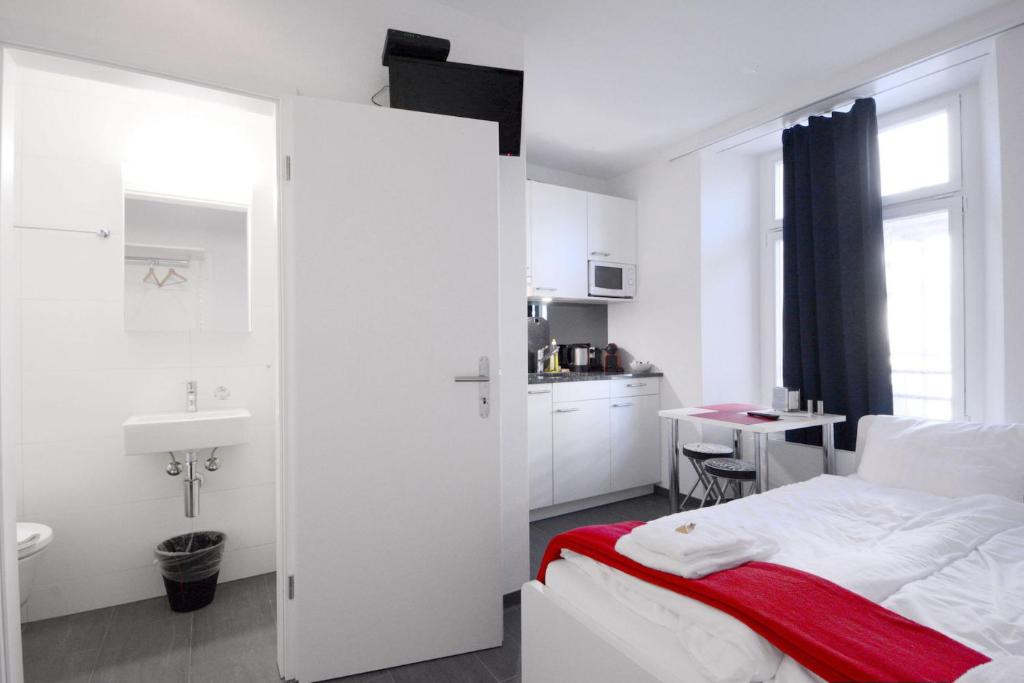 a white bedroom with a bed and a sink at HITrental Station Apartments in Lucerne