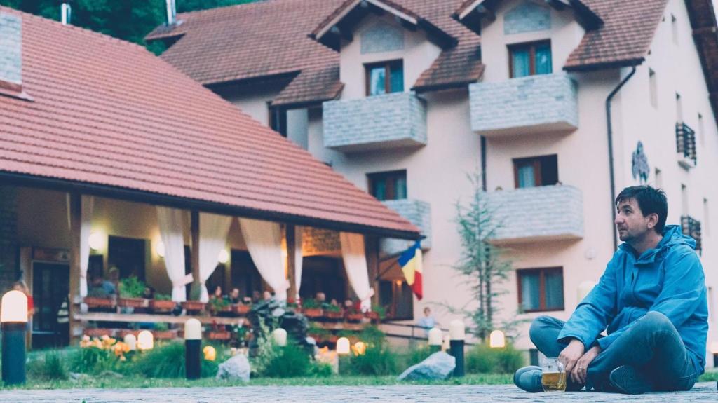 a man sitting on the ground in front of a house at Rocker's Inn in Sasca Montană