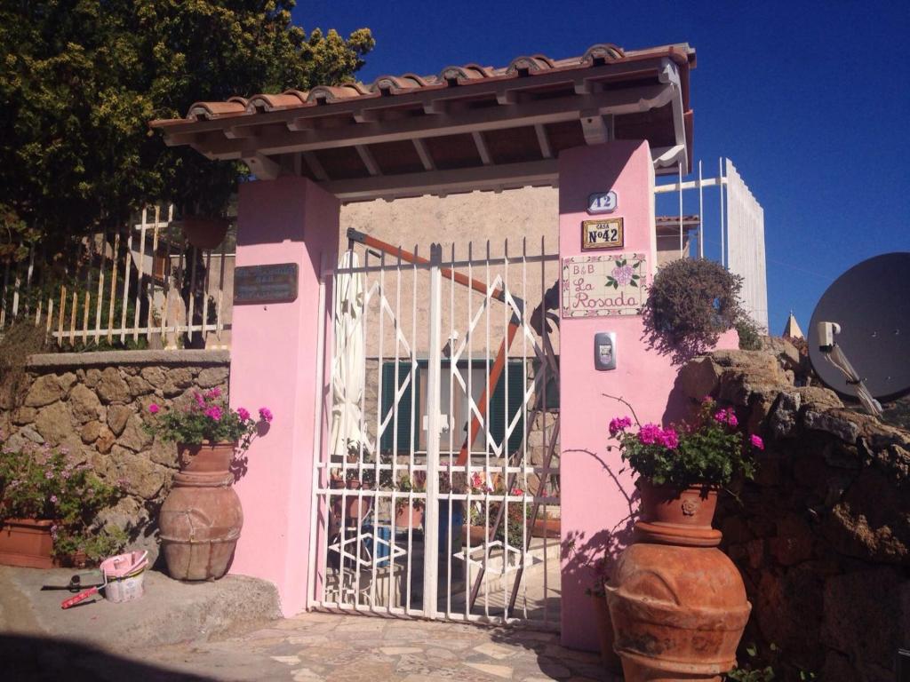 uma casa rosa com um portão e algumas flores em La Rosada em Giglio Porto