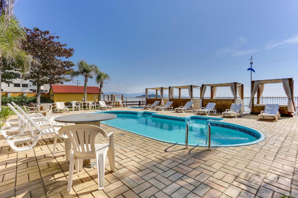 uma piscina com cadeiras brancas e uma mesa e uma mesa e cadeiras em Canasvieiras Hotel em Florianópolis