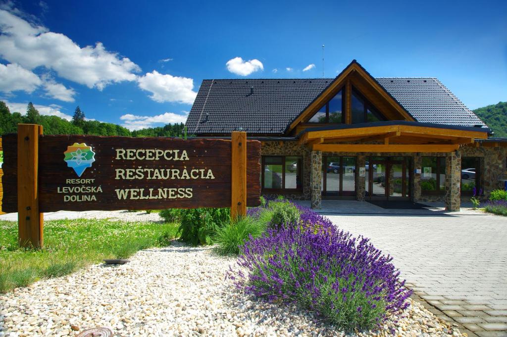 a sign in front of a building with purple flowers at Resort Levočská Dolina in Levoča