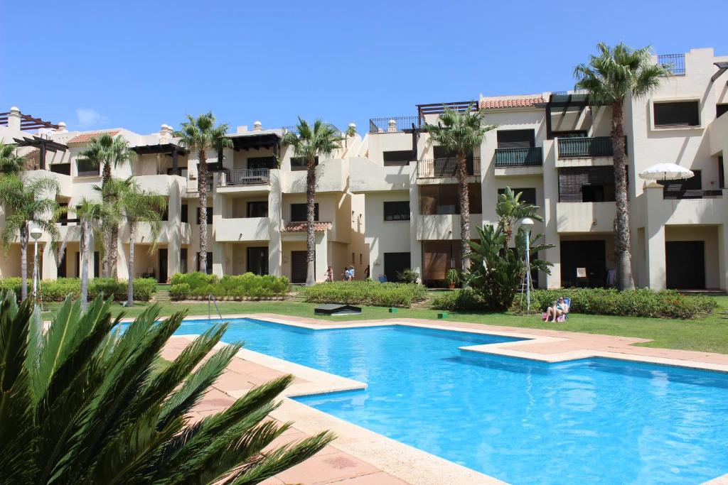 RodaにあるRoda Golf & Beach Resort, Murciaのヤシの木が茂る建物の前にあるスイミングプール