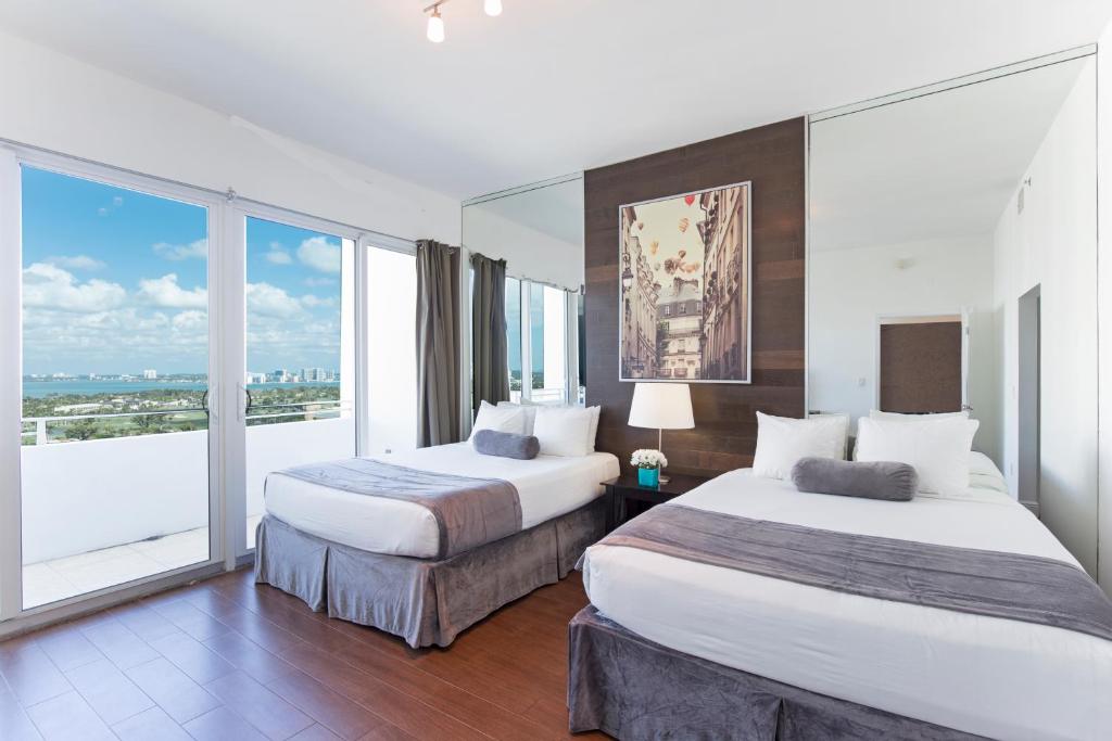 two beds in a hotel room with a large window at New Point Miami Beach Apartments in Miami Beach