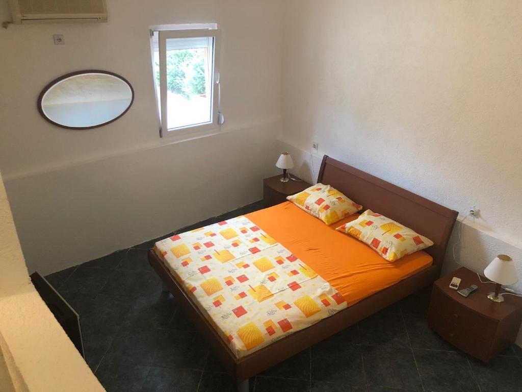 een slaapkamer met een bed met een oranje deken en een spiegel bij Apartmani Pavicevic in Podgorica