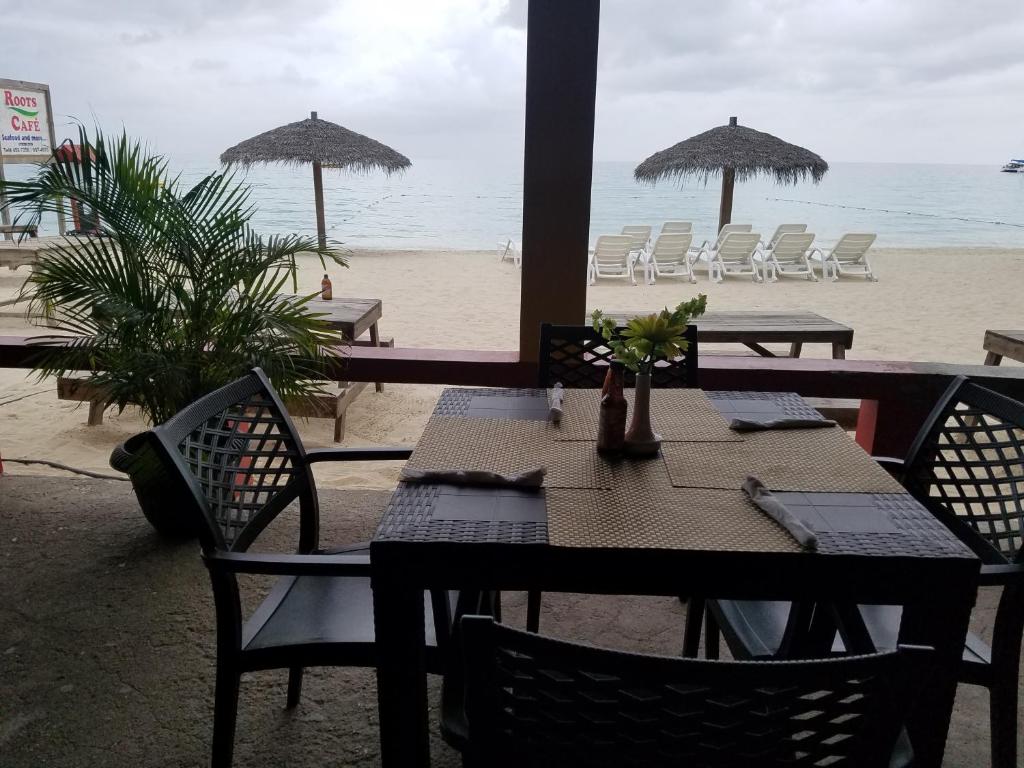a table and chairs on a beach with umbrellas at Roots Cafe Rooms in Negril