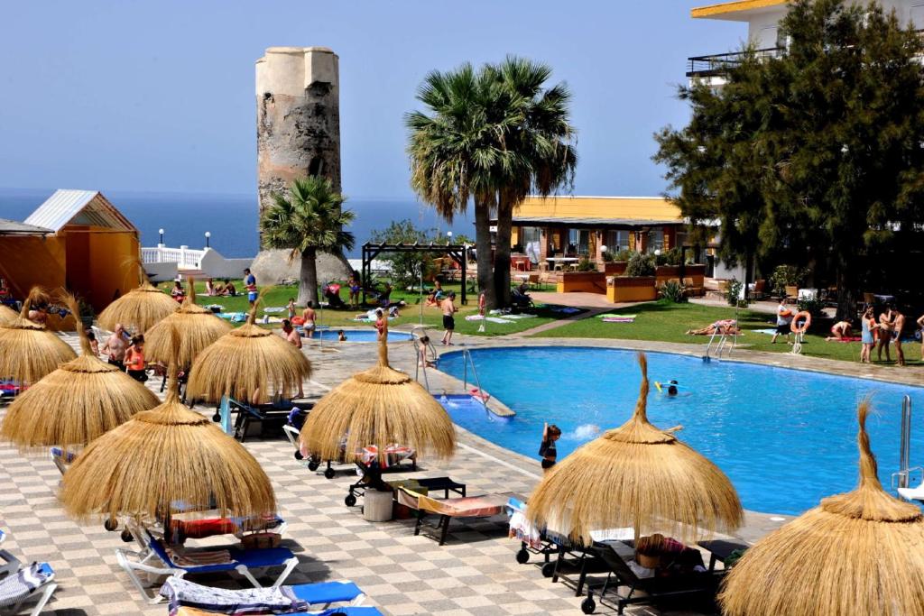 un resort con piscina e ombrelloni di paglia di Hotel Salobreña Suites a Salobreña