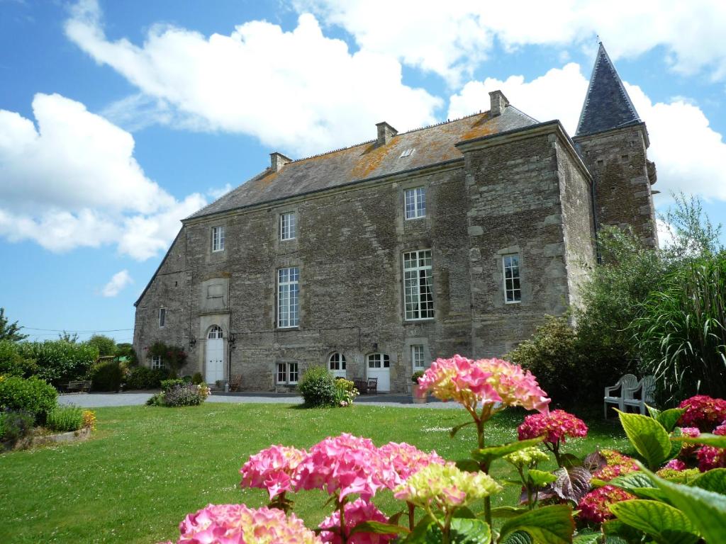 un antiguo edificio de piedra con flores en primer plano en MANOIR de la RIVIERE, en Géfosse-Fontenay