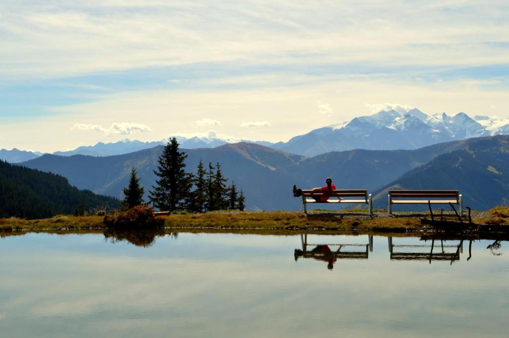 a person sitting on a bench next to a lake at Hotel Gamshag in Saalbach-Hinterglemm
