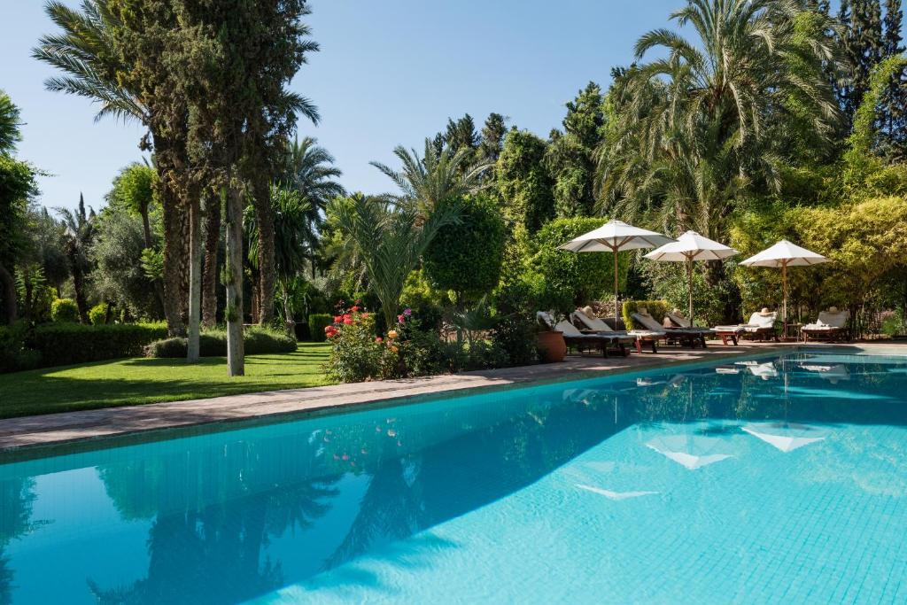 una piscina con palmeras y sombrillas en Dar Zemora, en Marrakech