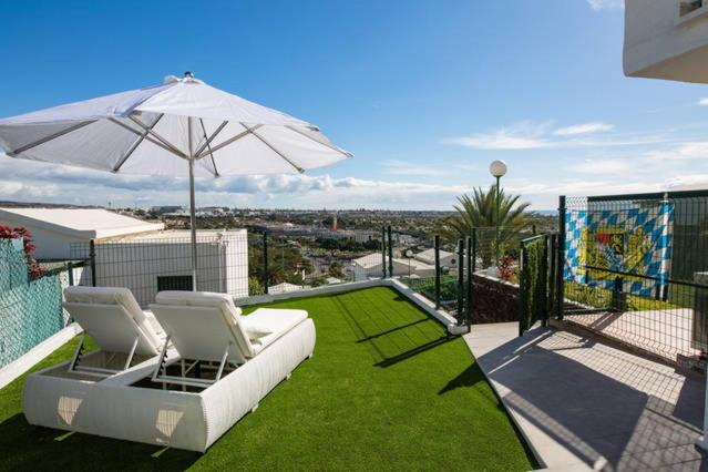 a patio with two chairs and an umbrella and grass at bungalow con gran terraza con vistas in Maspalomas