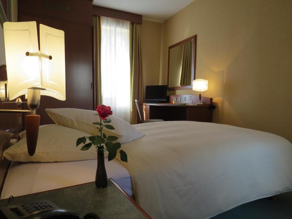a hotel room with a bed and a vase with a flower on a table at Hôtel du Port in Lausanne