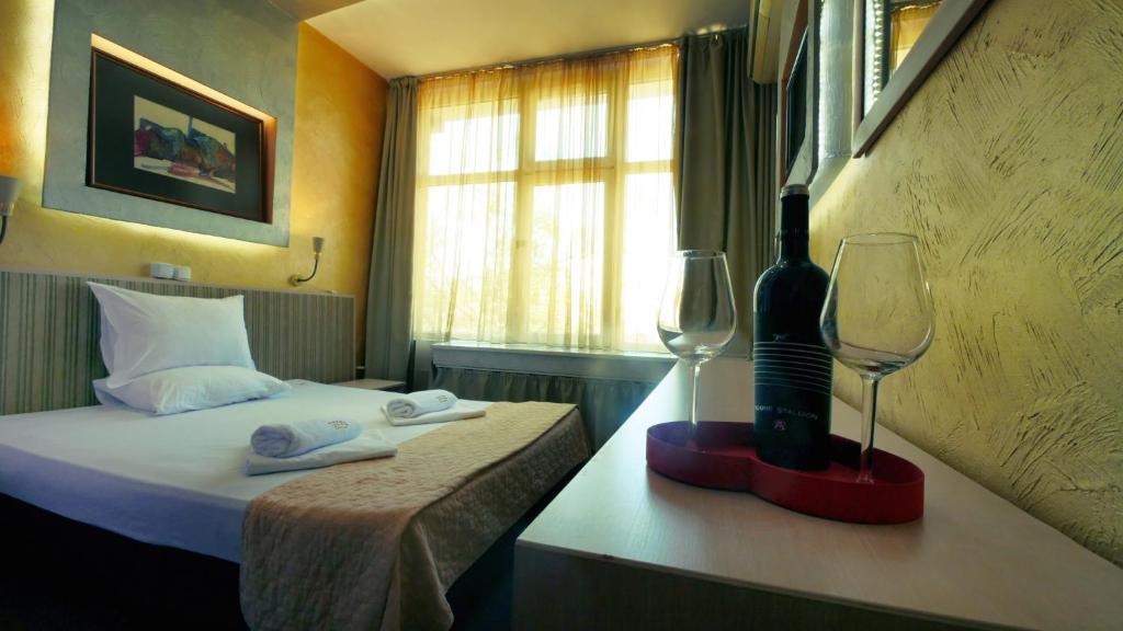 ソフィアにあるホテル アラビン セントラルのベッド1台とワイングラス2杯が備わるホテルルームです。