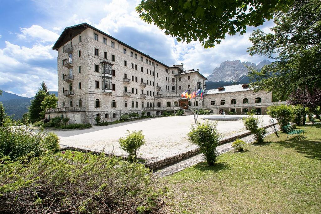 un grand bâtiment en pierre avec des montagnes en arrière-plan dans l'établissement TH Borca di Cadore - Park Hotel Des Dolomites, à Borca di Cadore
