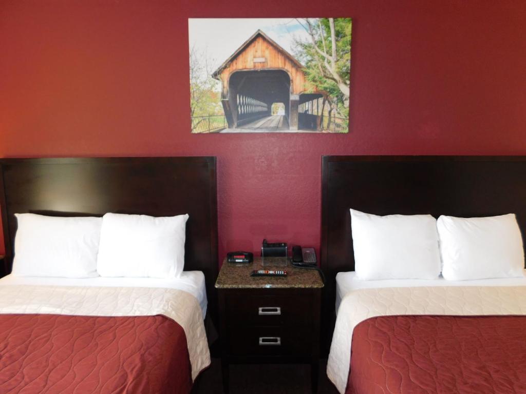 2 łóżka w pokoju hotelowym z czerwonymi ścianami w obiekcie The Covered Bridge Inn w mieście Brattleboro