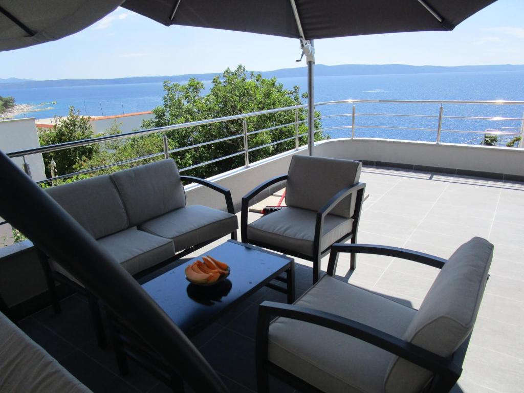 - un balcon avec 2 chaises, une table et un parasol dans l'établissement Apartmani Marinović, à Podgora