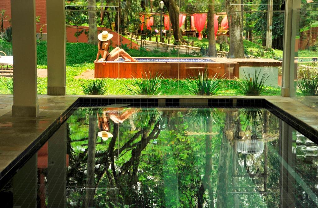 uma piscina no meio de um jardim com uma pessoa sentada num banco em Hotel Resort e Golfe Clube dos 500 em Guaratinguetá