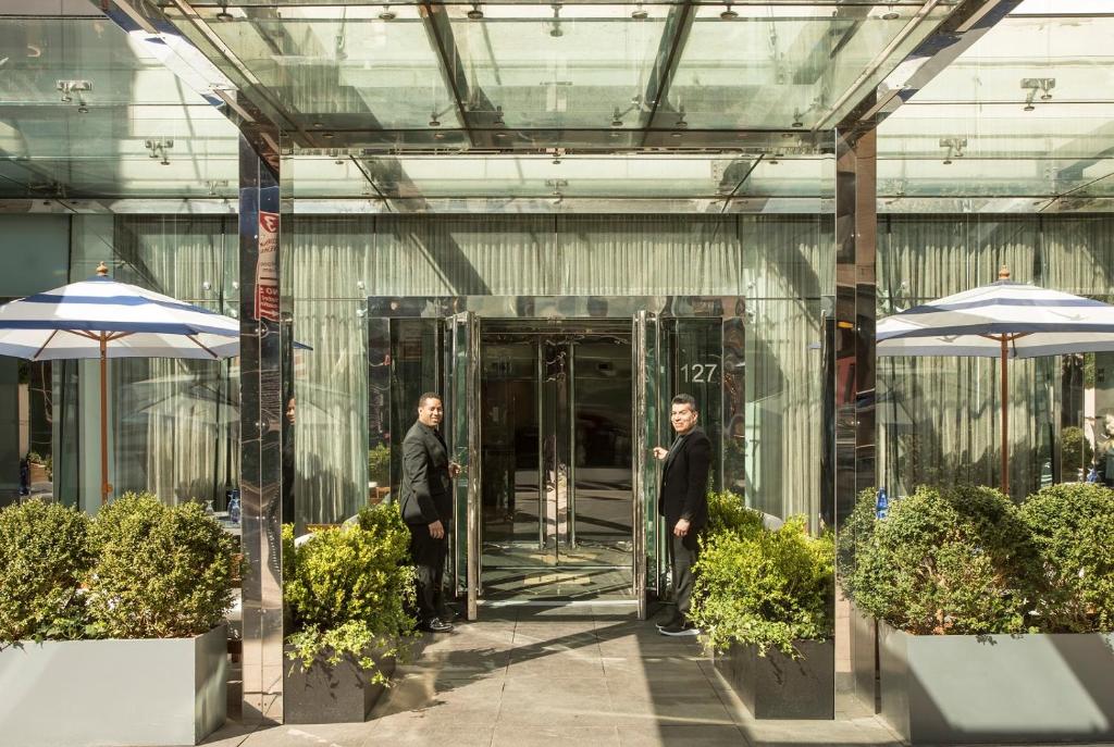 Dois homens a entrar num edifício de vidro com guarda-chuvas. em Hotel Hayden New York em Nova Iorque