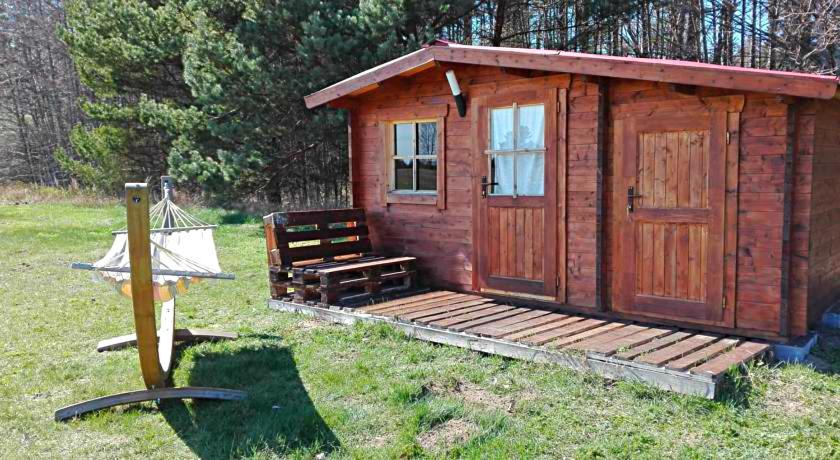 a small wooden cabin with a bench in the grass at SP camping Spāres Prieduļi in Nīca