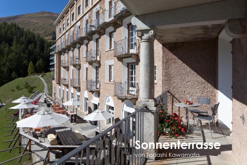 einen Balkon eines Gebäudes mit Tischen und Sonnenschirmen in der Unterkunft Hotel Castell in Zuoz