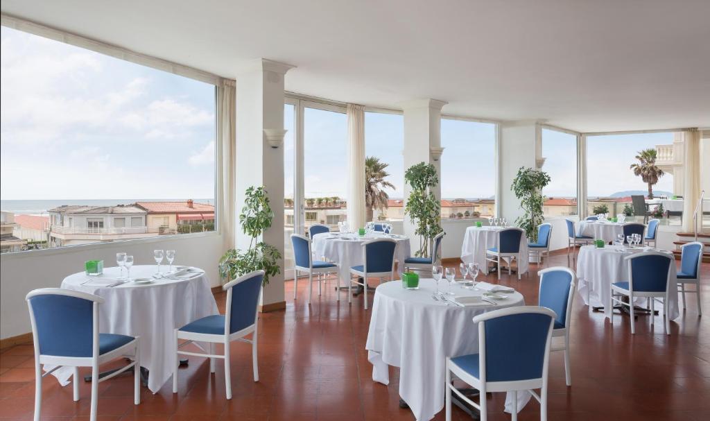a room with white tables and blue chairs and windows at Hotel Sina Astor in Viareggio