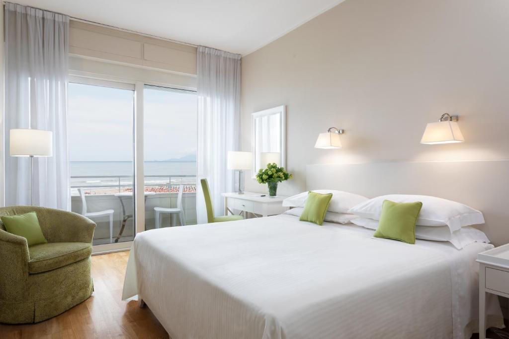 a white bedroom with a large bed and a chair at Hotel Sina Astor in Viareggio