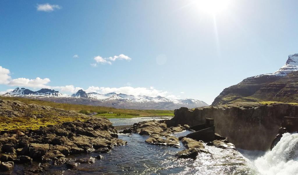 een rivier met een waterval en bergen op de achtergrond bij Fossardalur Guesthouse in Djúpivogur