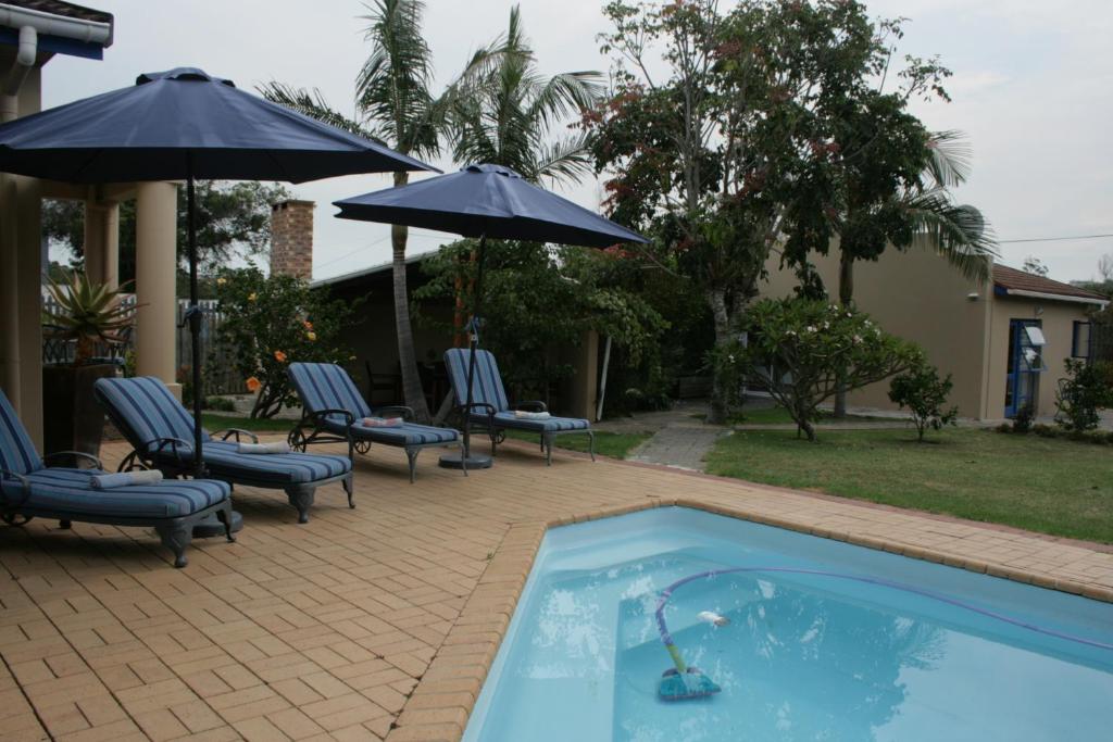 a pool with chairs and umbrellas next to a house at 113 on Robberg in Plettenberg Bay