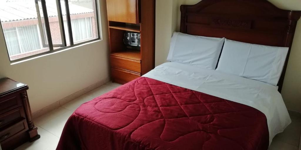 1 dormitorio con 1 cama con edredón rojo y ventana en Hostal Fontanar Prado, en Bogotá