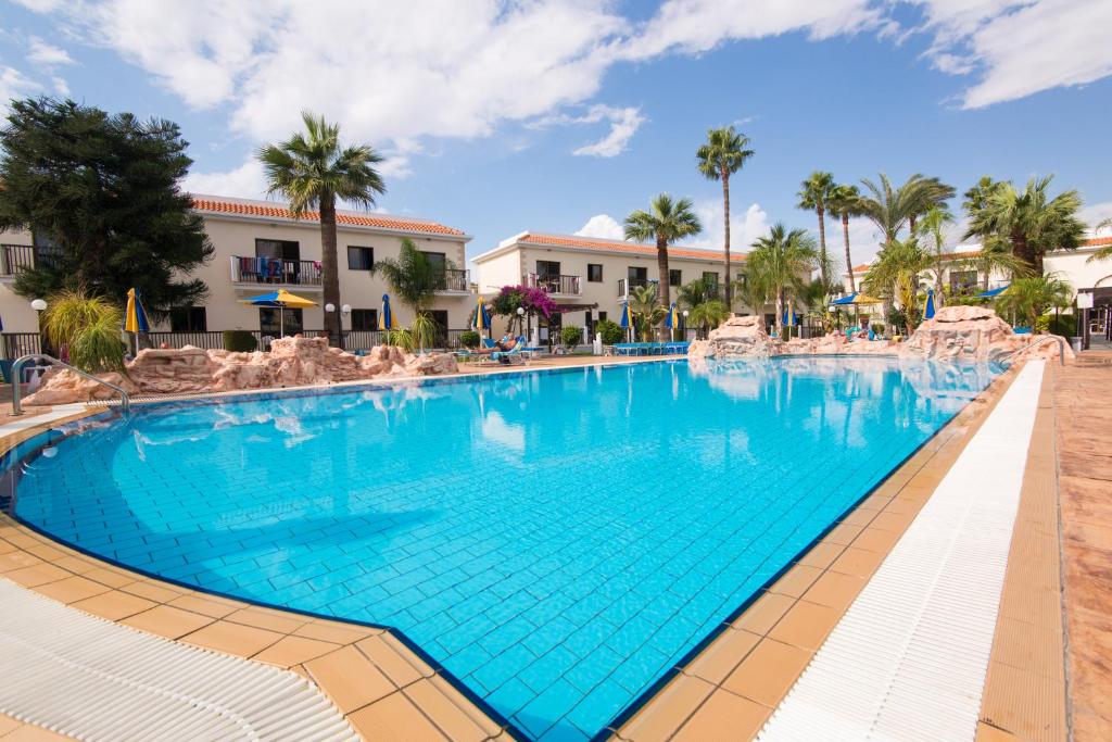 a swimming pool at a resort with chairs and palm trees at Loutsiana Deluxe Apts in Ayia Napa