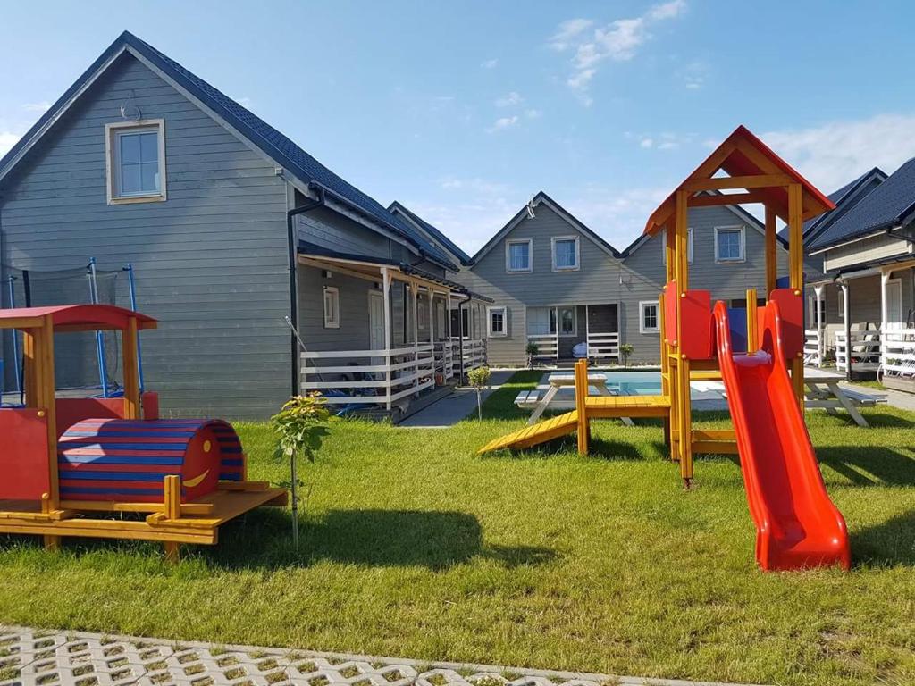 un patio con parque infantil frente a las casas en Domki Gościniak, en Rewal