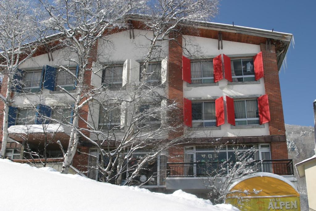 an apartment building with red shuttered windows in the snow at Villa Alpen in Yamanouchi