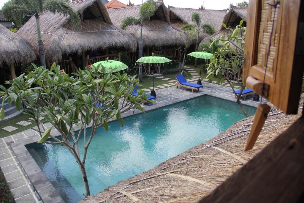 una piscina en un complejo con sillas y sombrillas en The Calmtree Bungalows en Canggu