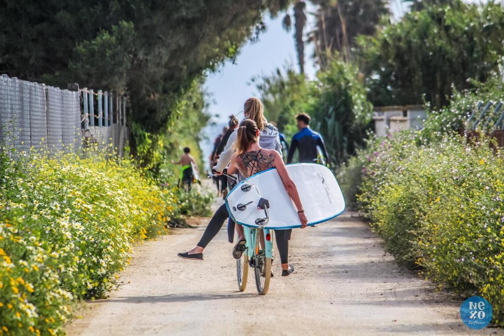 a group of people riding bikes down a path with a surfboard at Nexo Surf House in El Palmar